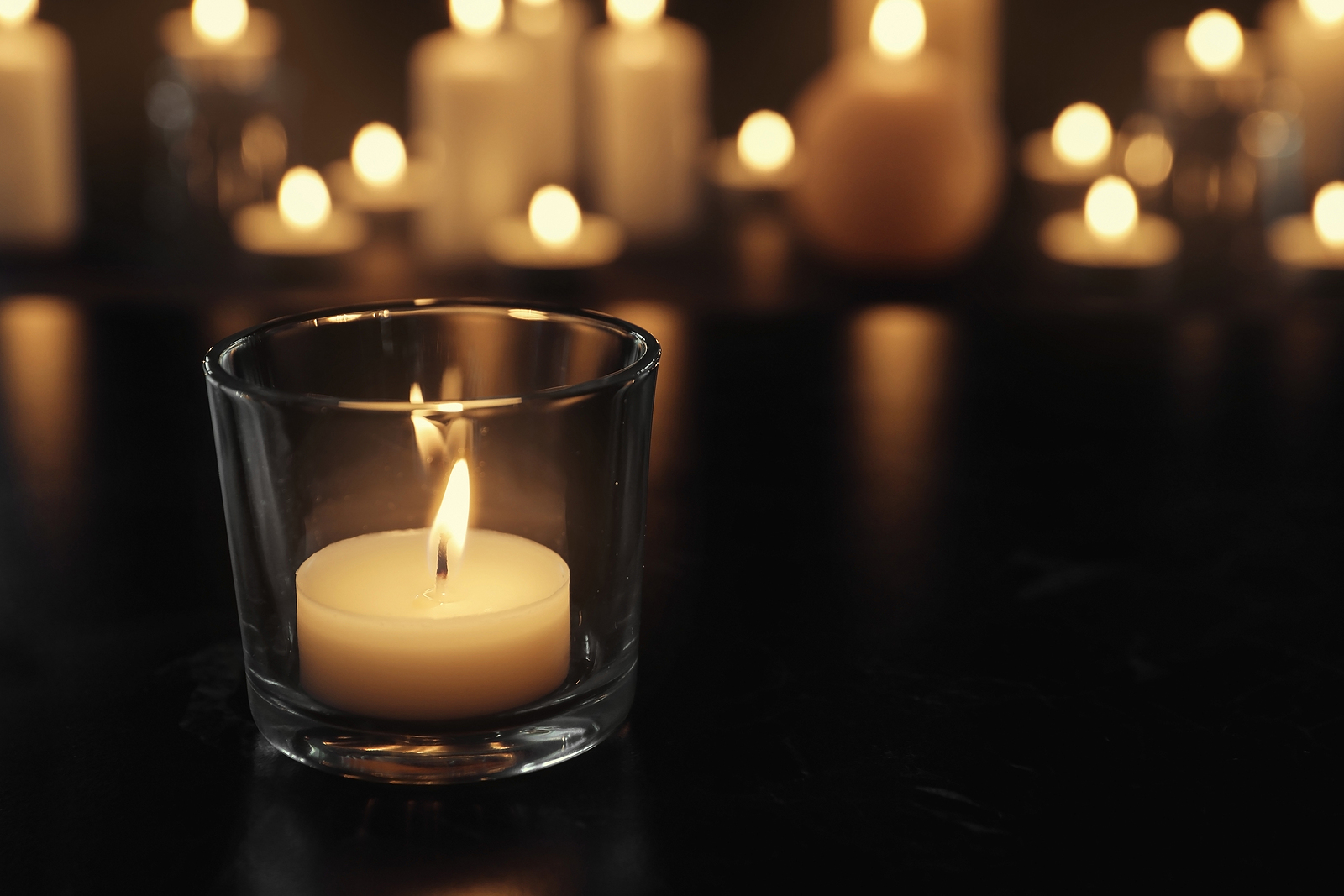 Burning candle on table in darkness